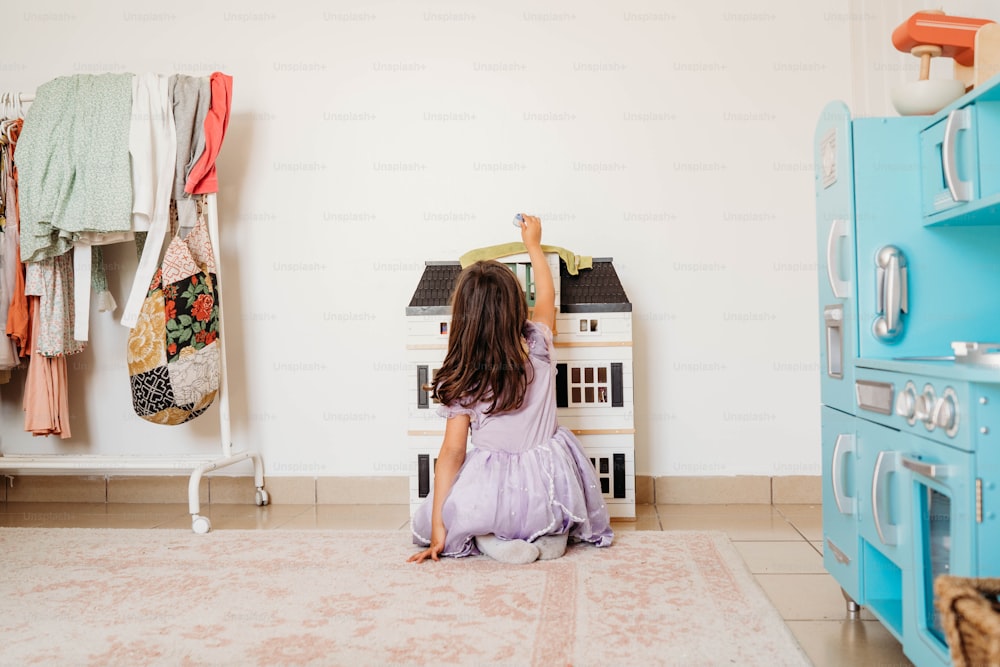 a little girl sitting on the floor in front of a doll house