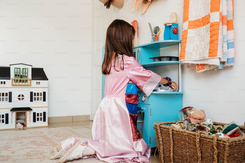 a little girl in a pink dress standing in front of a toy house
