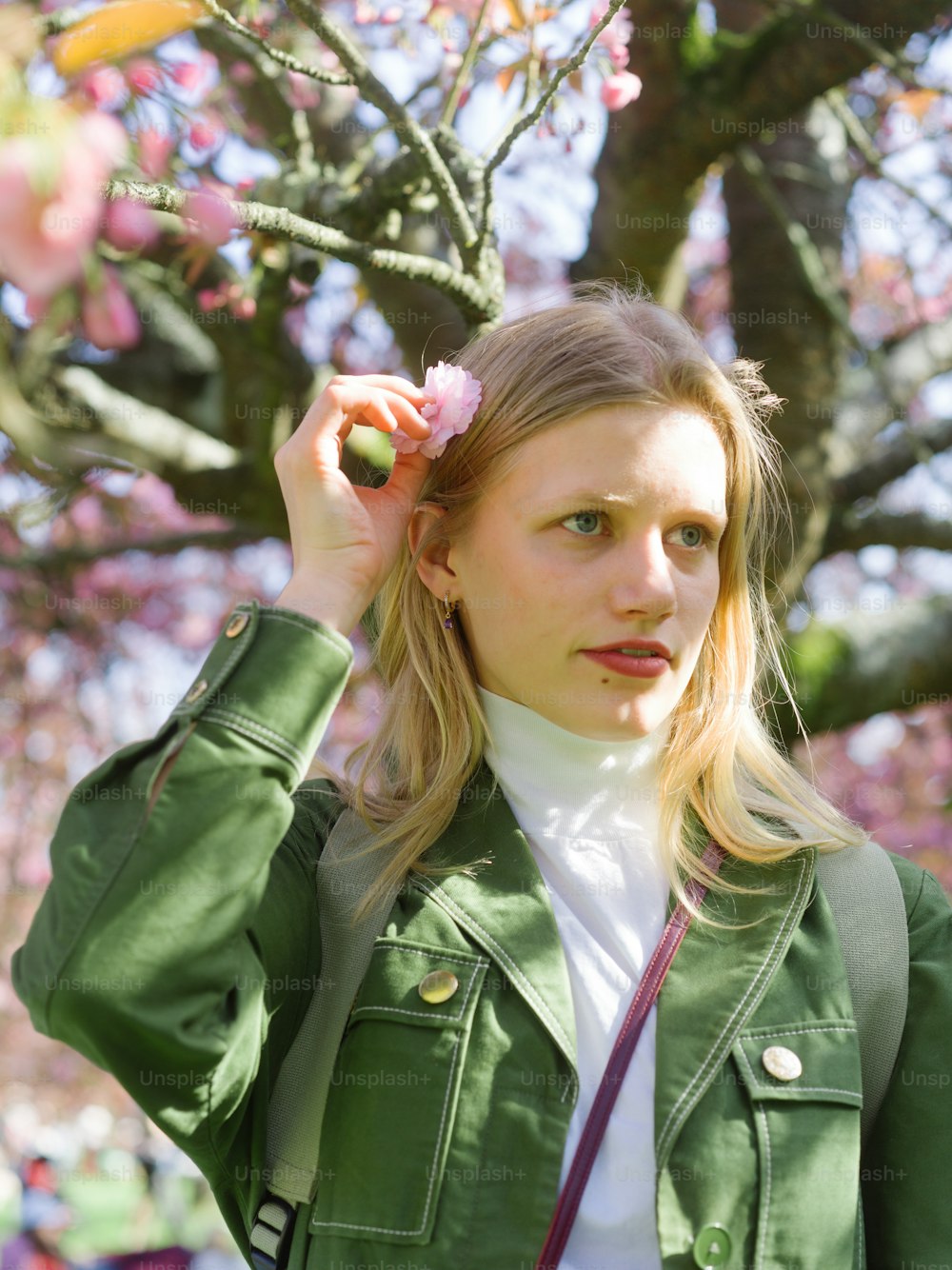 a woman in a green jacket is holding a flower in her hair