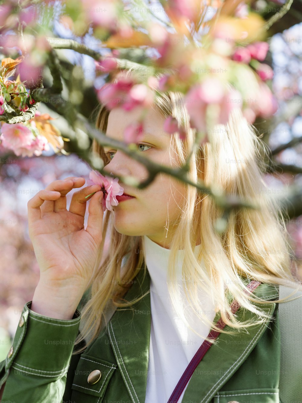 a woman in a green jacket smelling a flower
