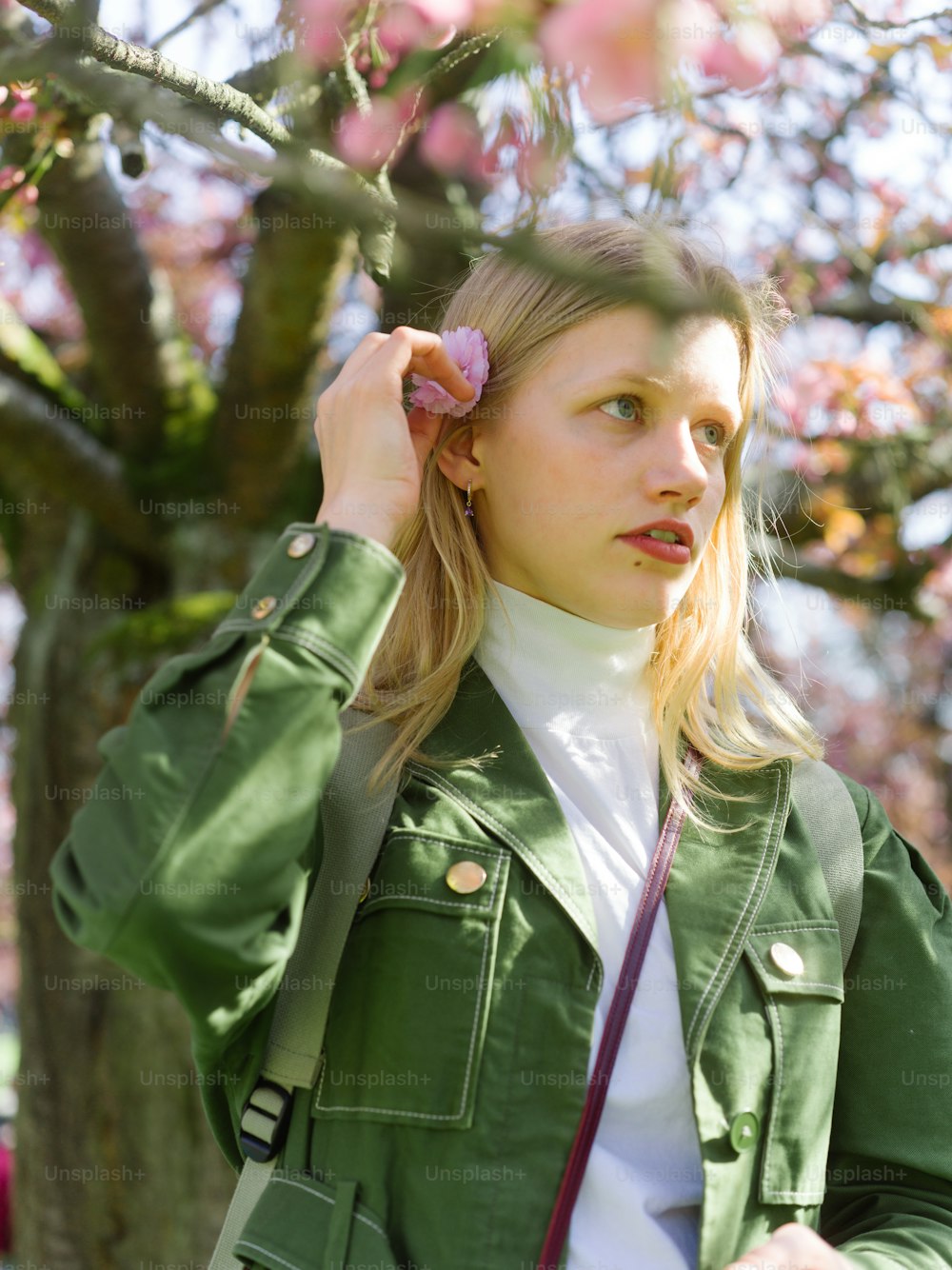 a woman in a green jacket holding a pink flower