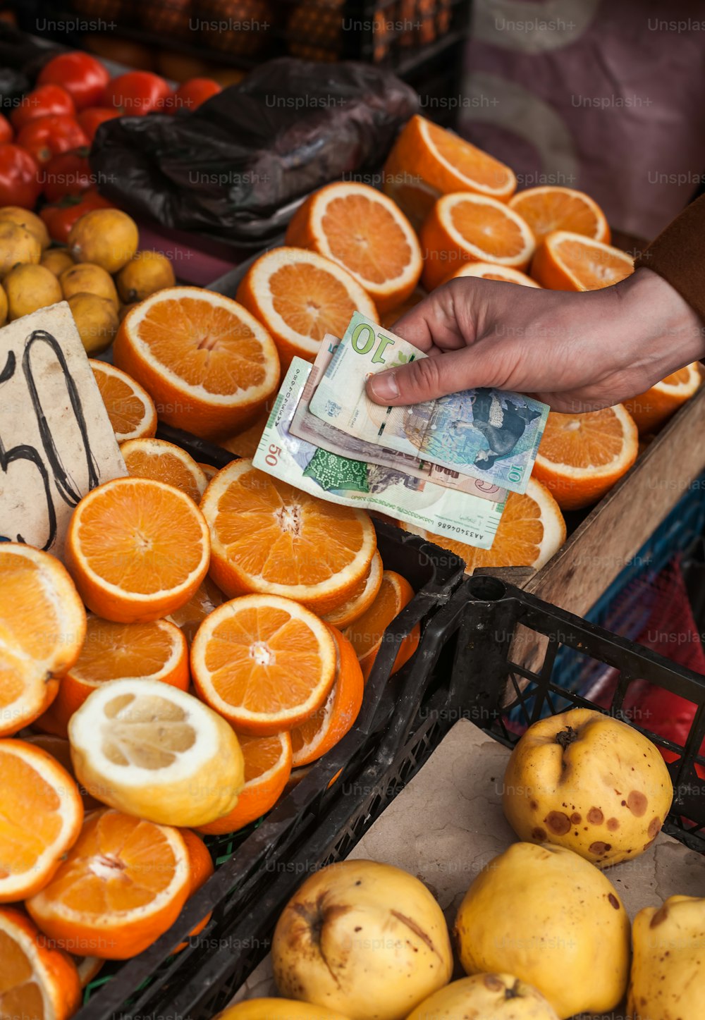 a person's hand holding money over a pile of oranges