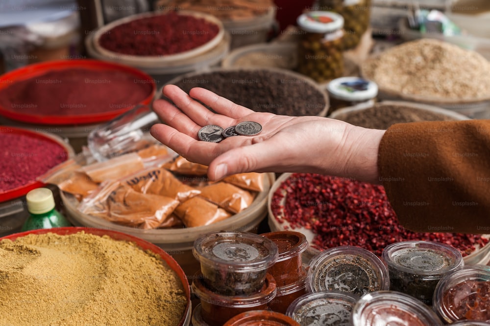 a person's hand reaching for a coin in front of a variety of spices