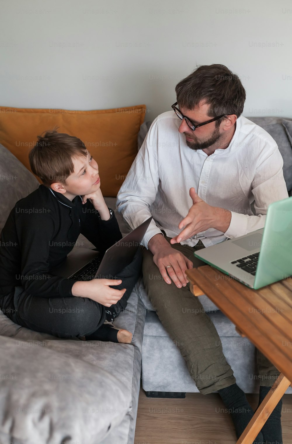 Un hombre y un niño sentados en un sofá mirando una computadora portátil