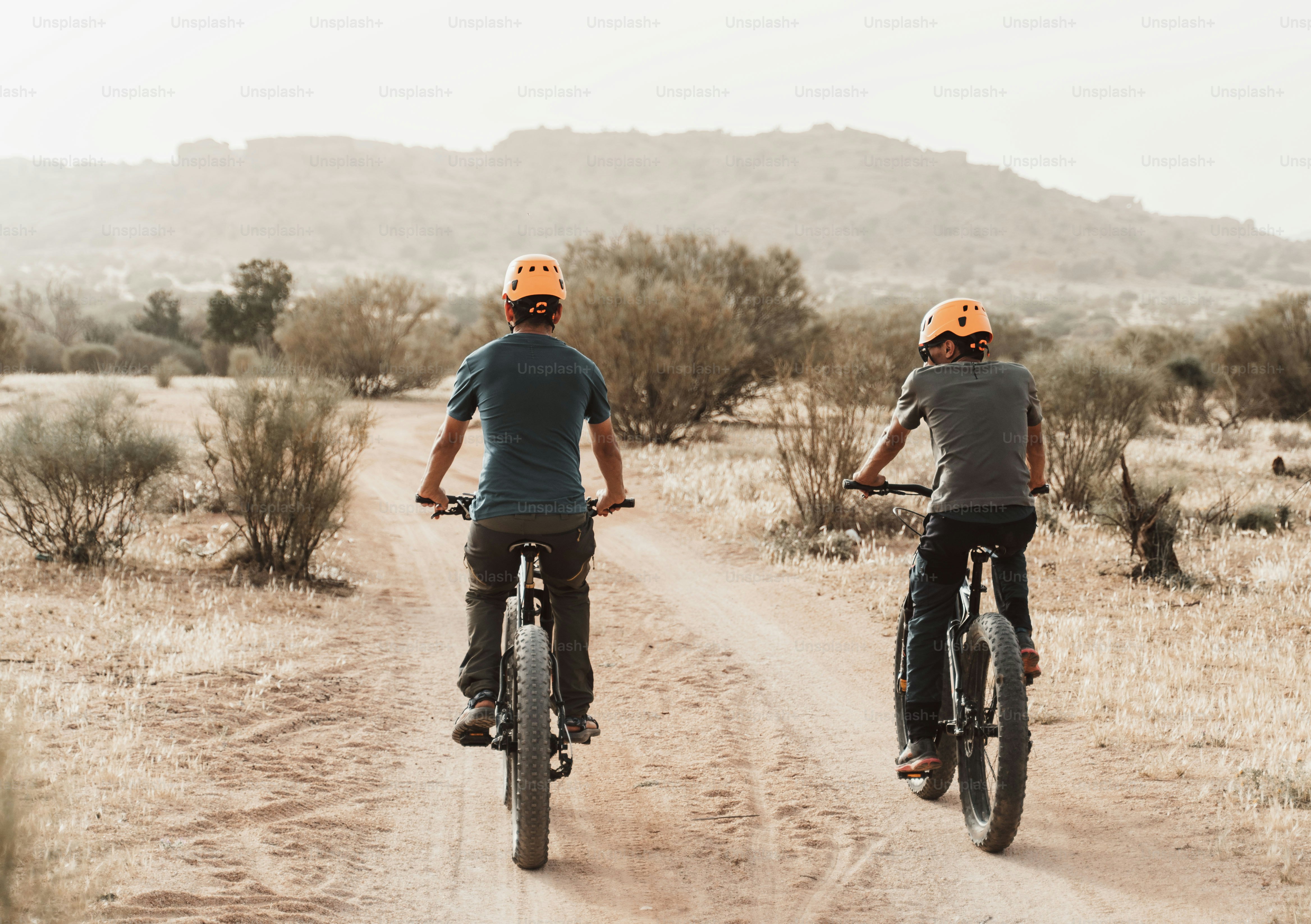 a couple of people riding bikes down a dirt road