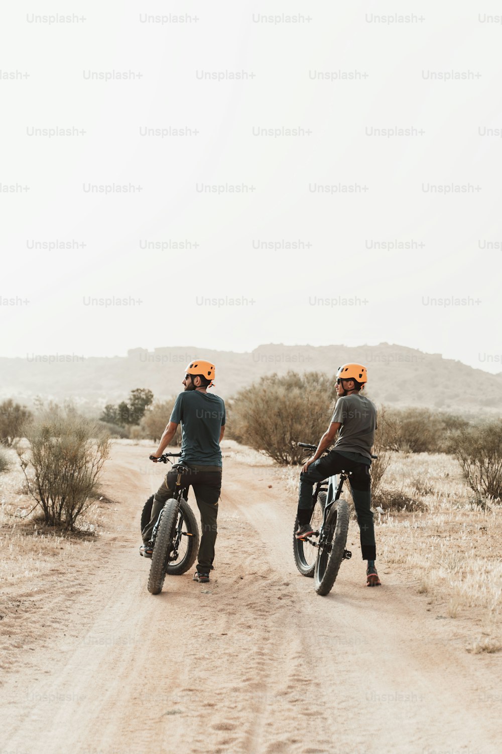 a couple of men riding bikes down a dirt road