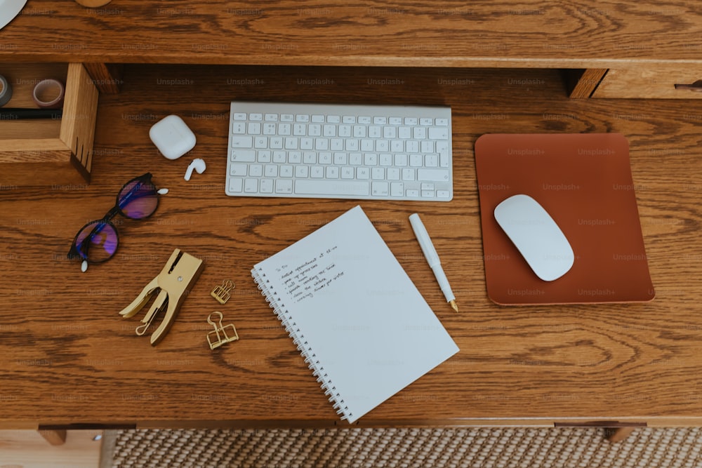 una scrivania con tastiera, mouse, occhiali e un blocco note