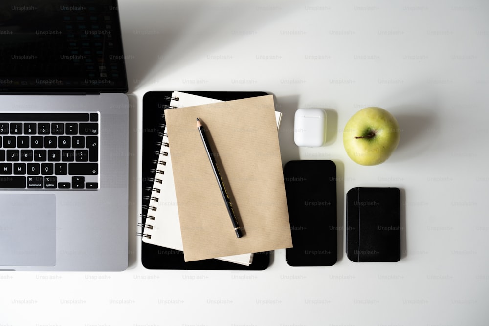 um caderno, caneta e maçã sentados em uma mesa ao lado de um laptop