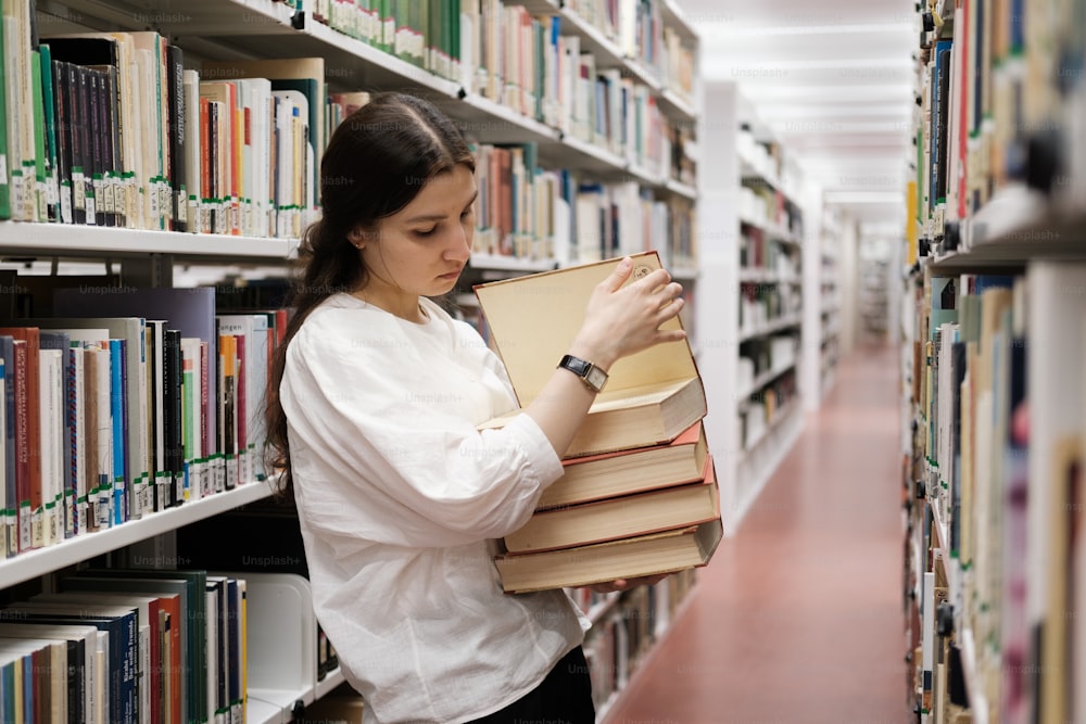 uma mulher segurando uma pilha de livros em uma biblioteca