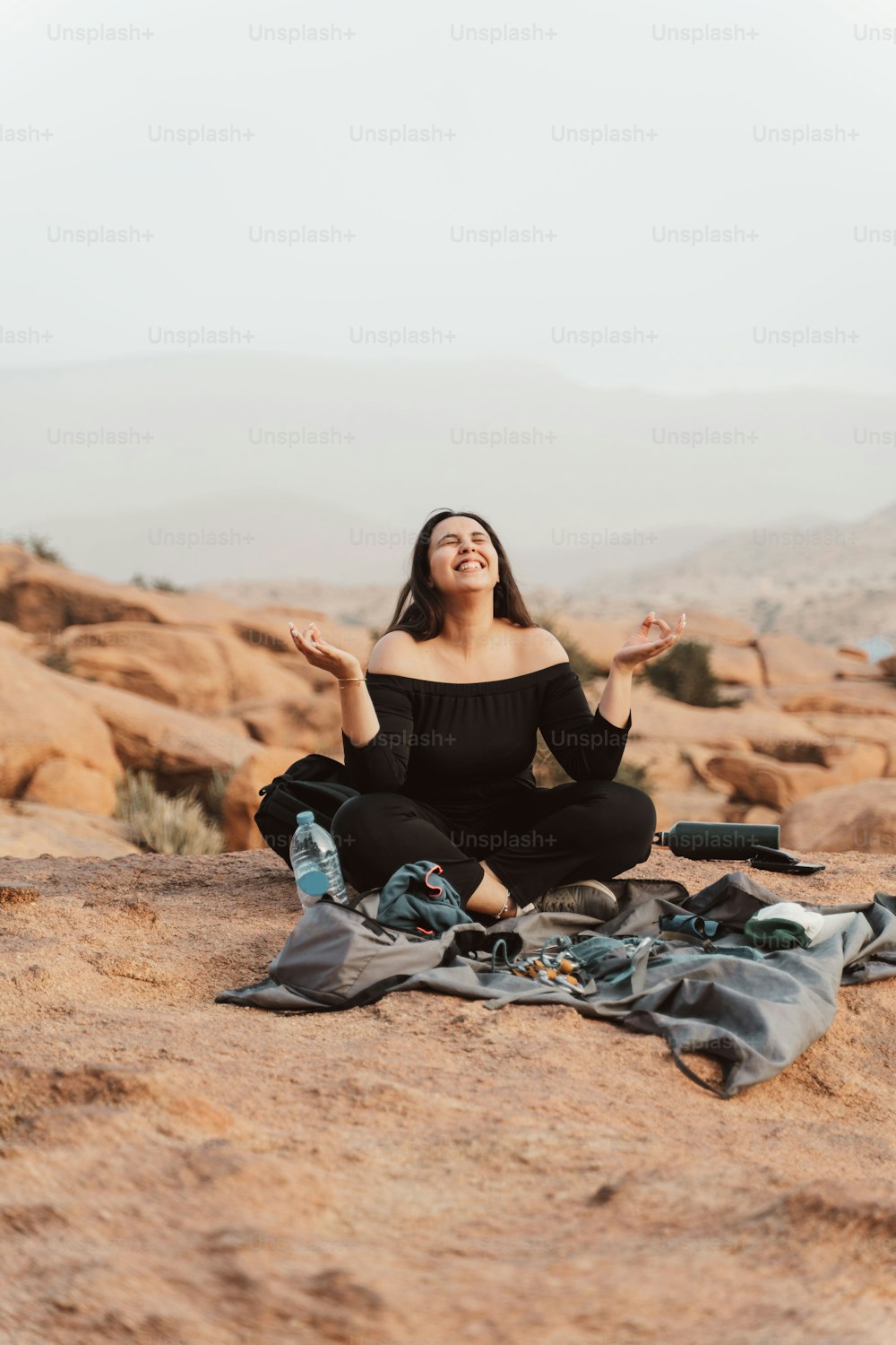 a woman in a black top is sitting on a blanket in the desert
