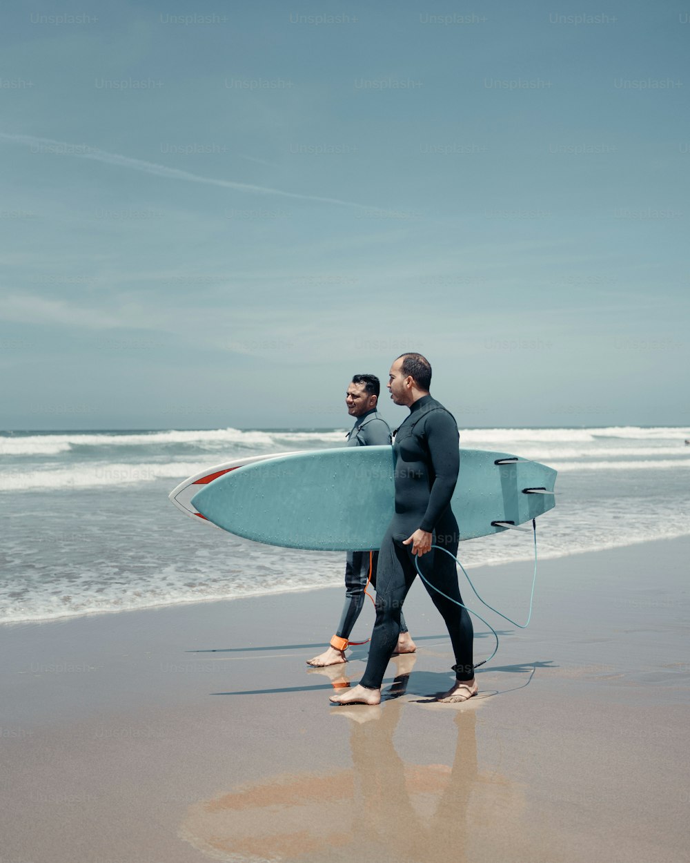 two men walking on the beach with a surfboard