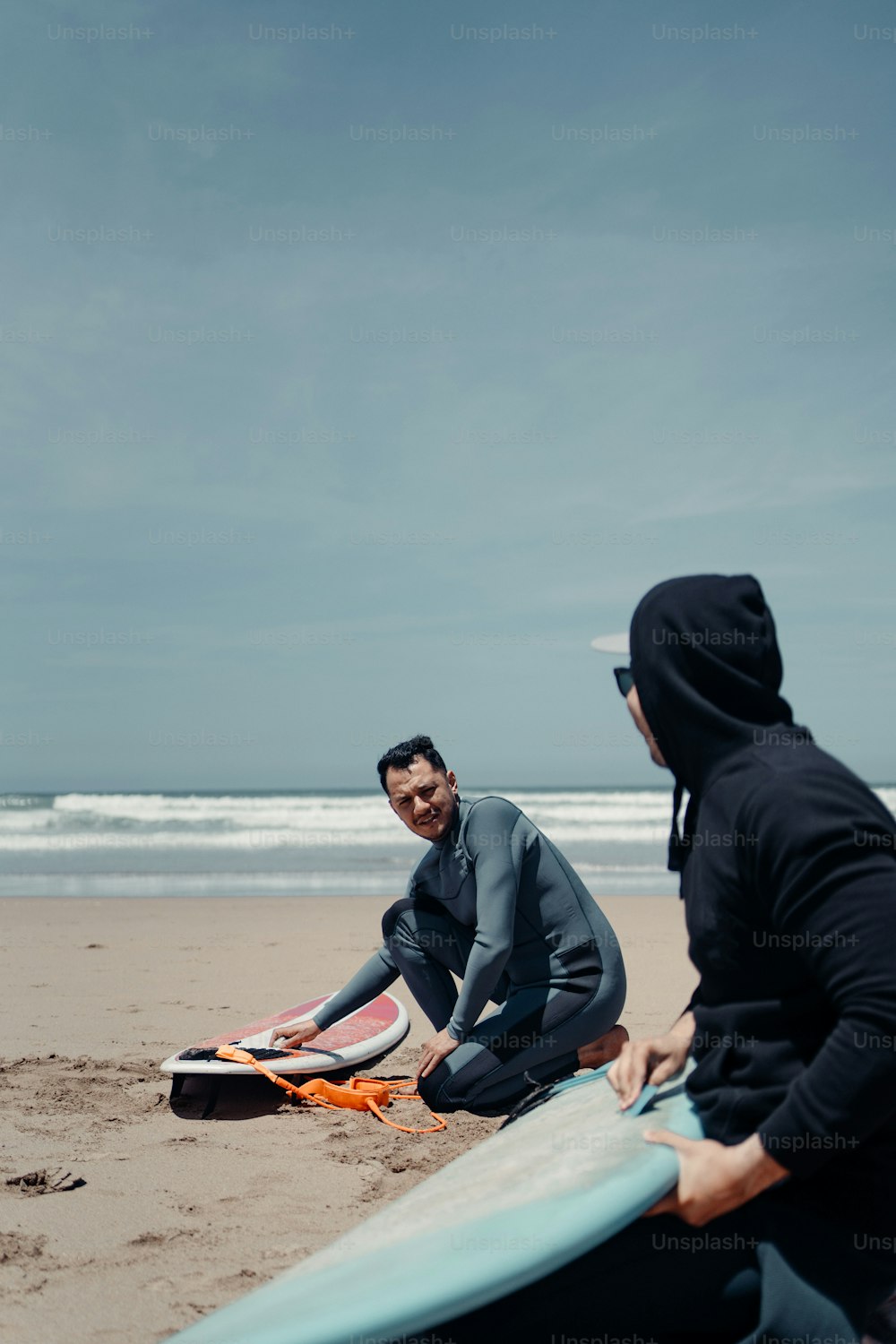 two people sitting on the beach with surfboards