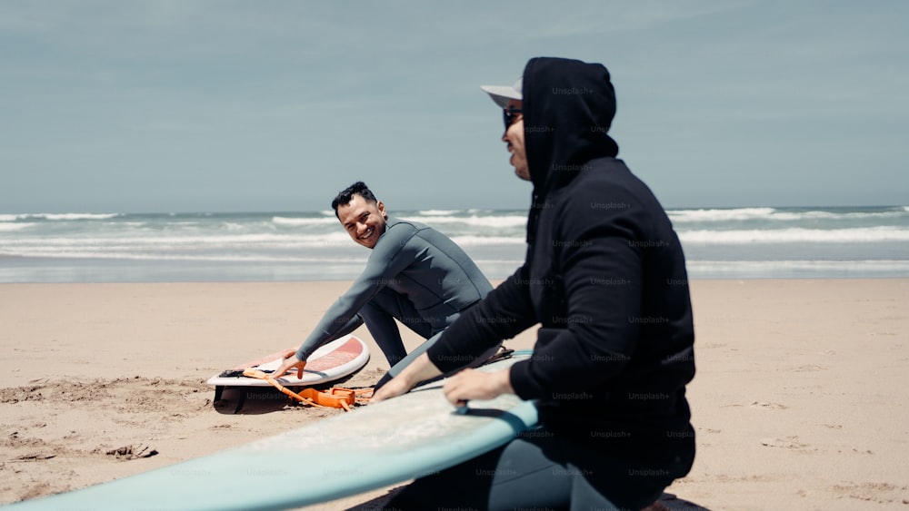 a couple of men sitting on top of a sandy beach