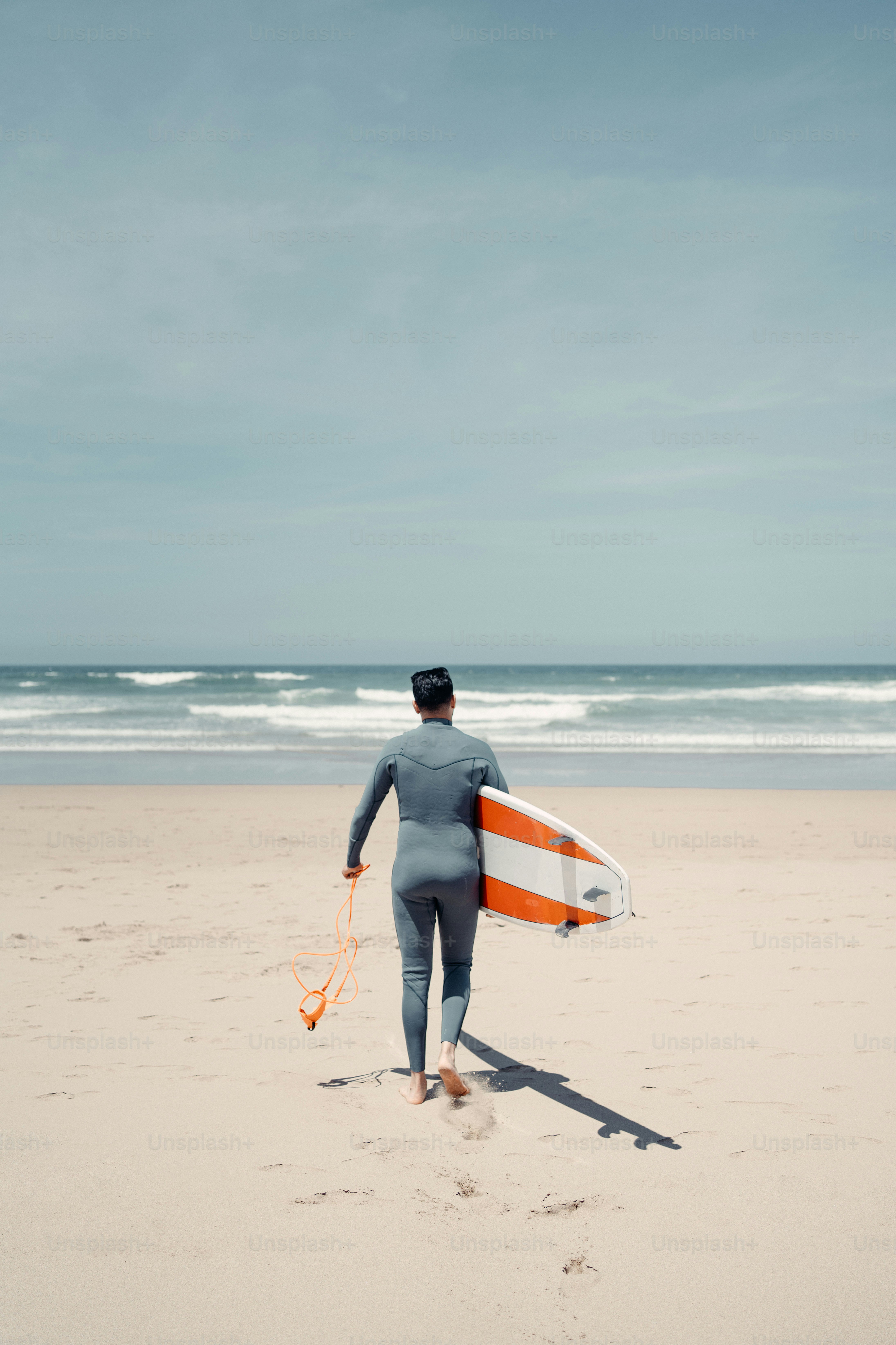 a man walking on a beach holding a surfboard