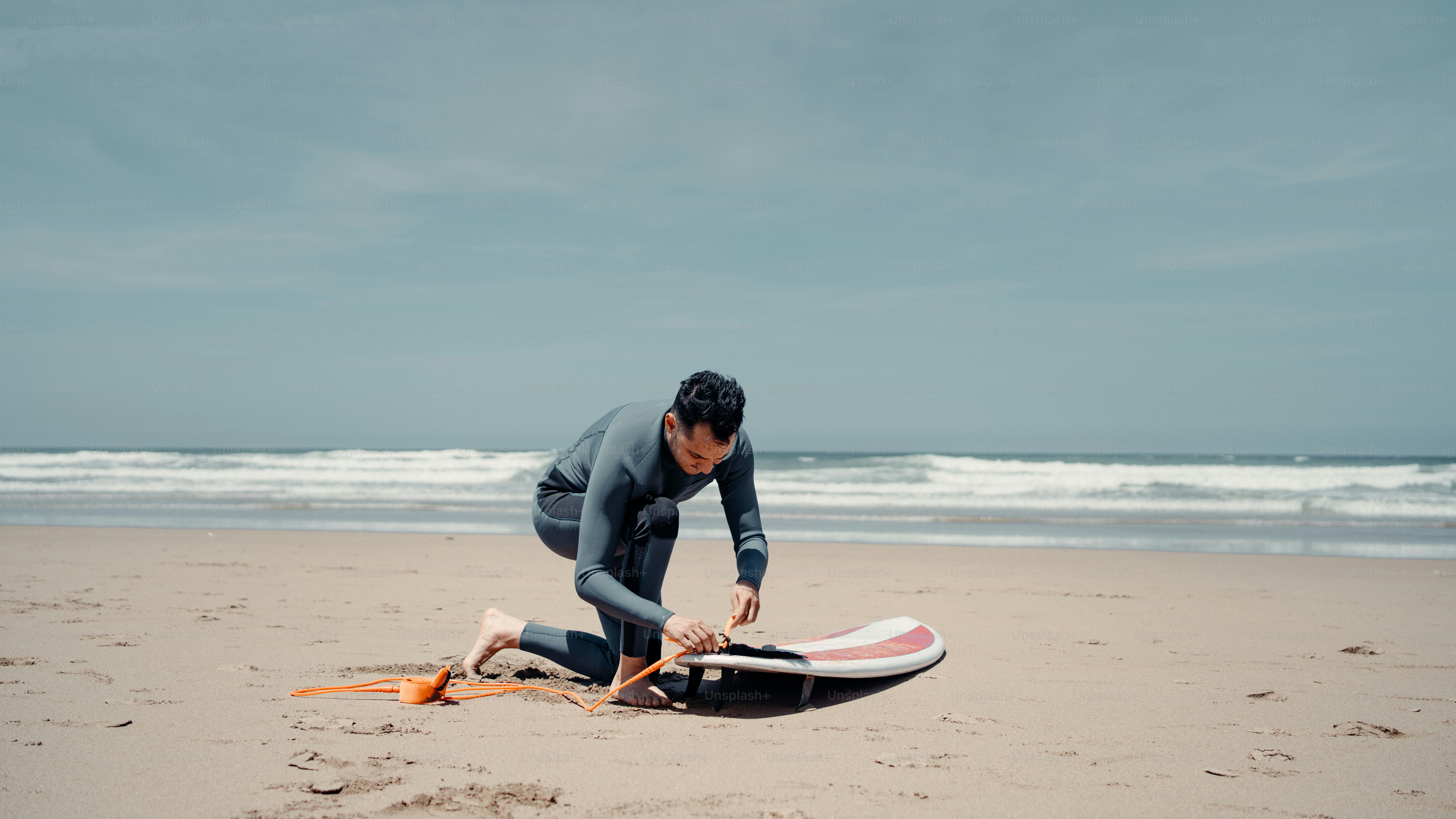 a man in a wet suit on a beach with a surfboard