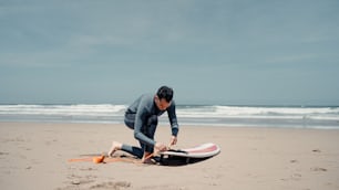 Un hombre con traje de neopreno en una playa con una tabla de surf