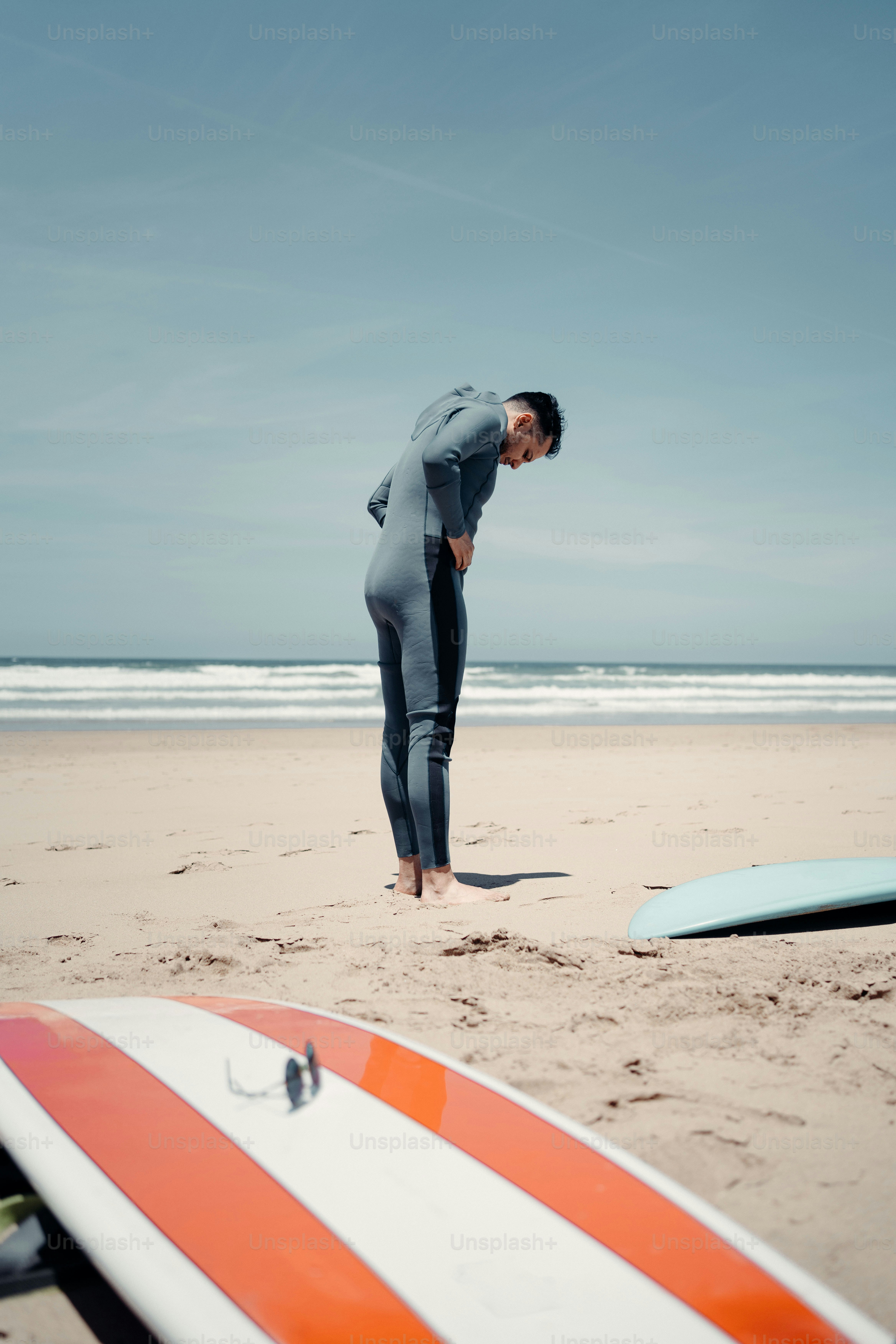 a man standing on a beach next to a surfboard