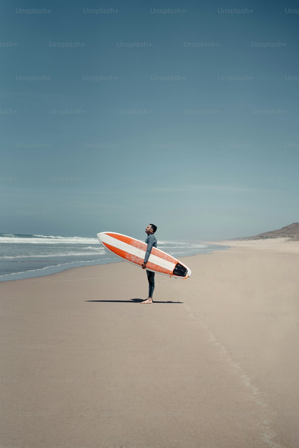 Un uomo che tiene una tavola da surf in cima a una spiaggia sabbiosa