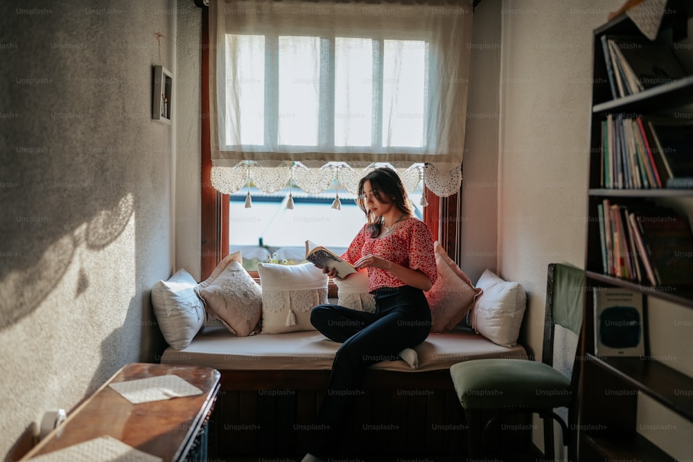 a woman sitting on a window seat reading a book