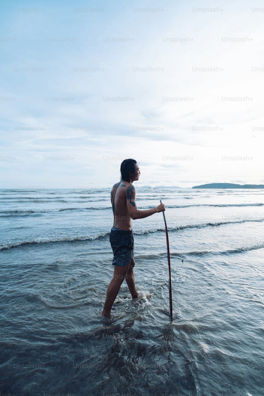a man standing in the ocean holding a stick