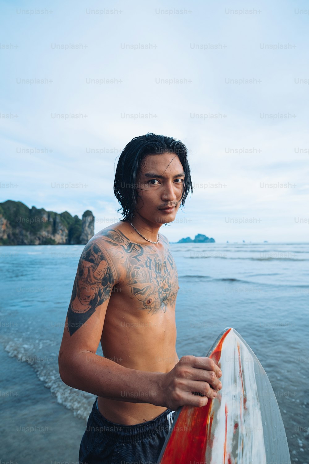 Un uomo a torso nudo che tiene una tavola da surf sulla spiaggia