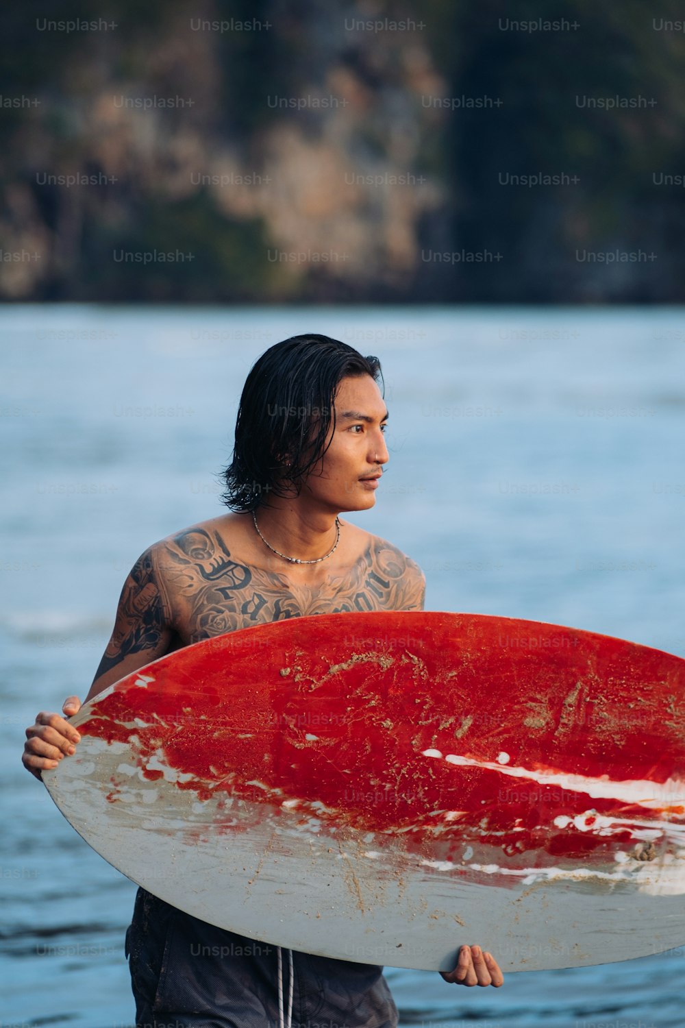 a man holding a red and white surfboard on top of a body of water
