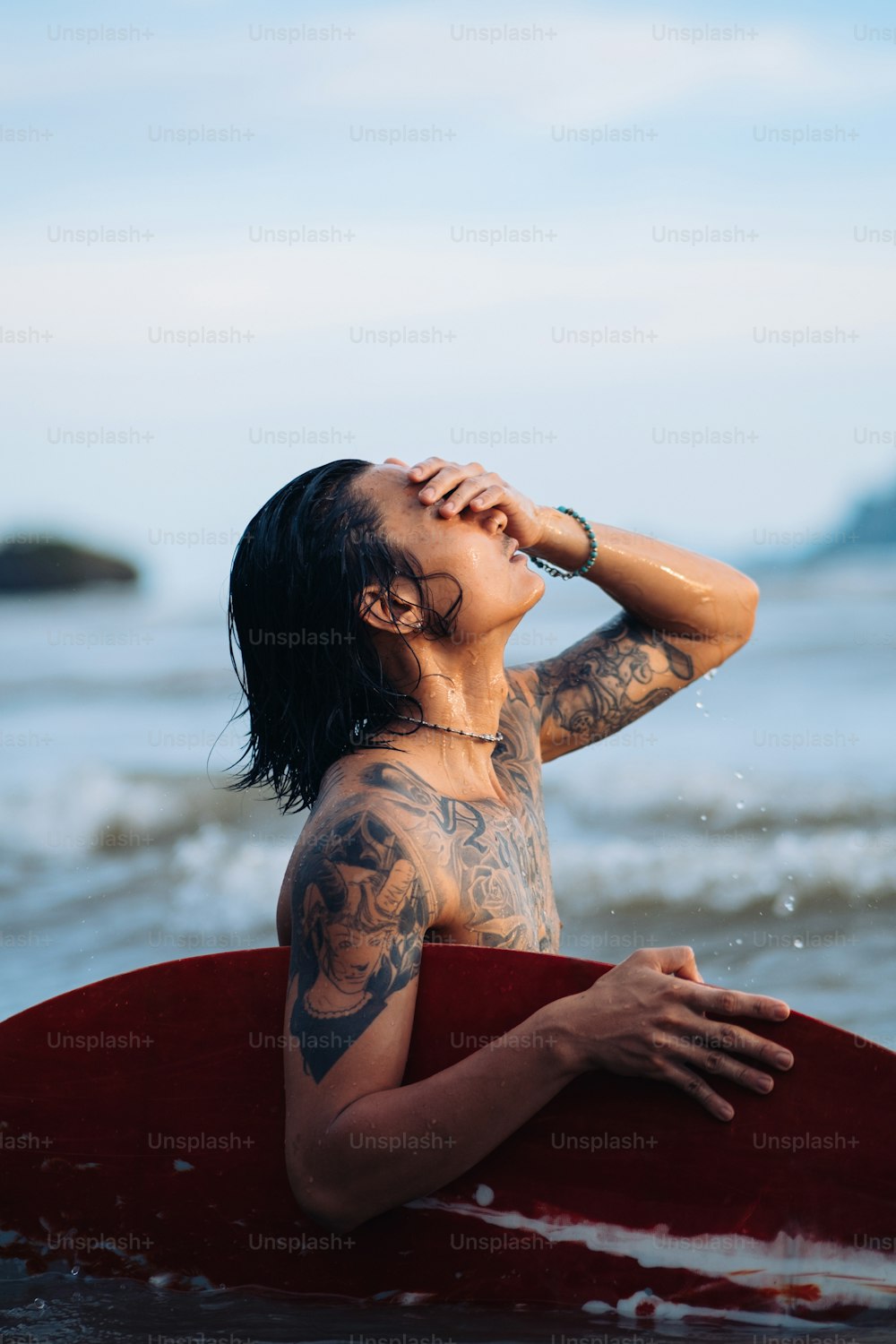 a man with tattoos on his body sitting on a surfboard