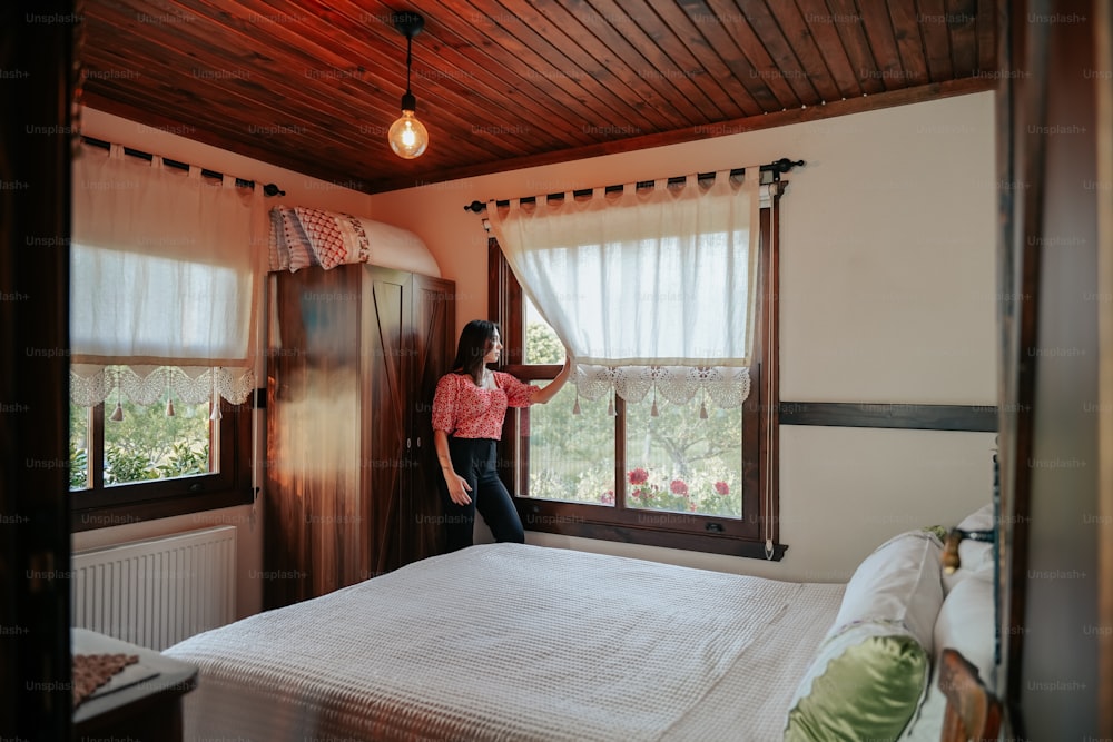 a woman standing in front of a window in a bedroom