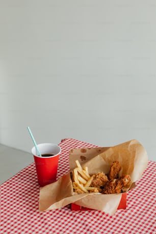 a red and white checkered table with a basket of fries and a cup of