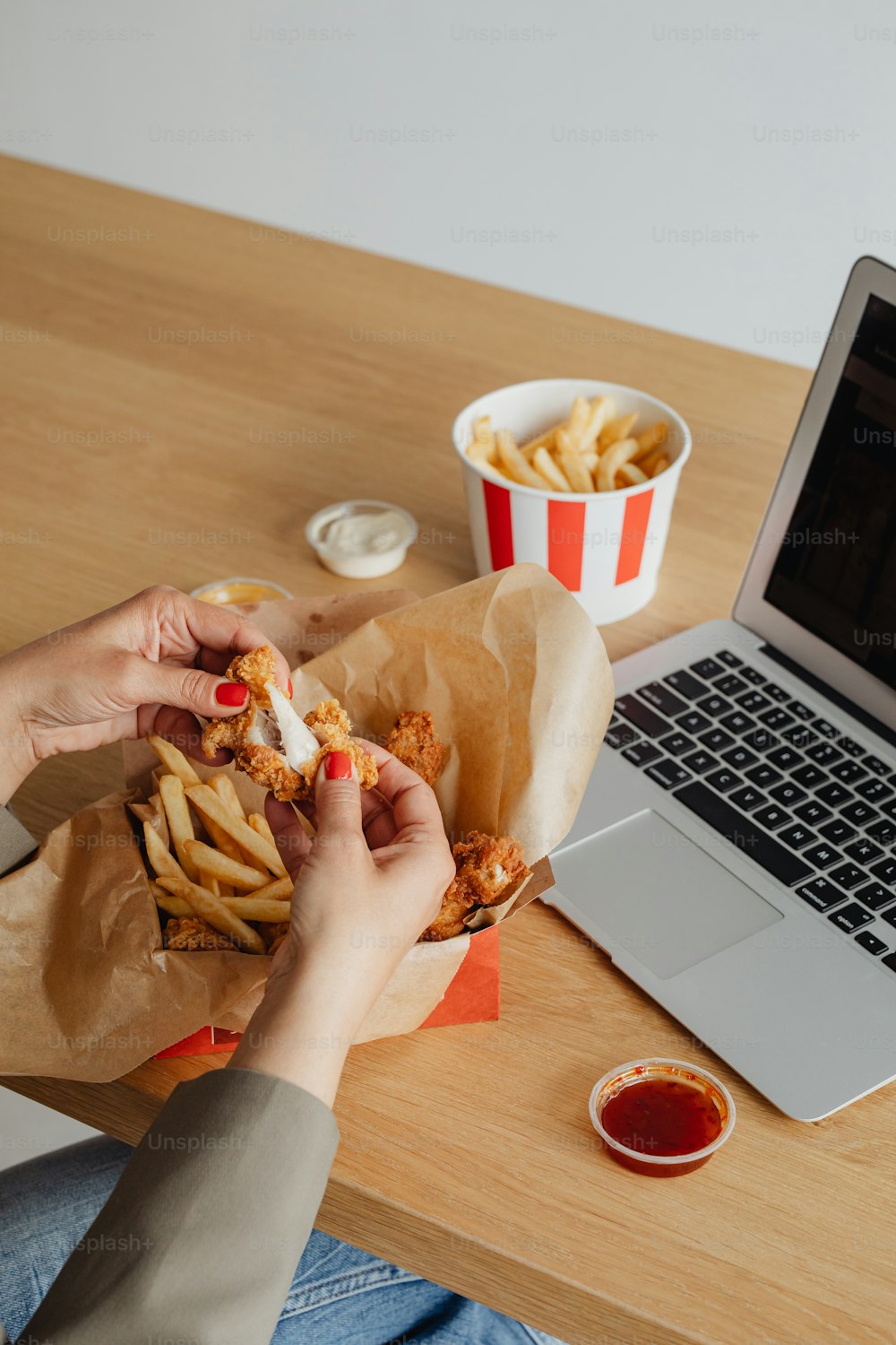 eine Person, die an einem Tisch mit einem Korb mit Essen vor einem Laptop sitzt