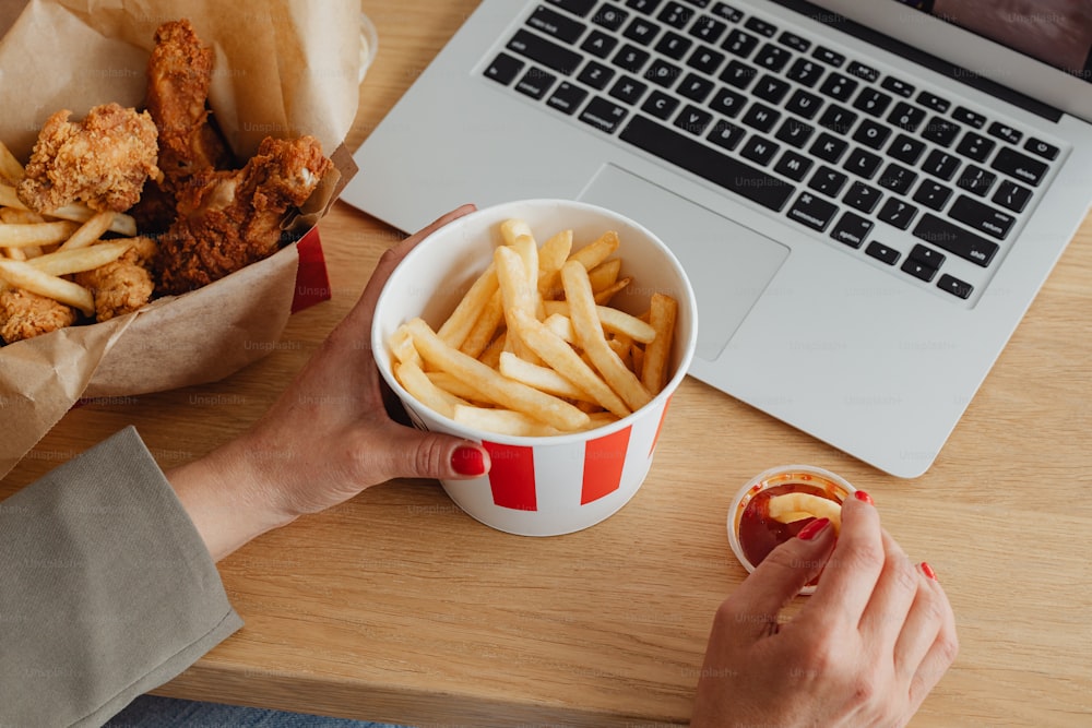 a person holding a cup of fries in front of a laptop