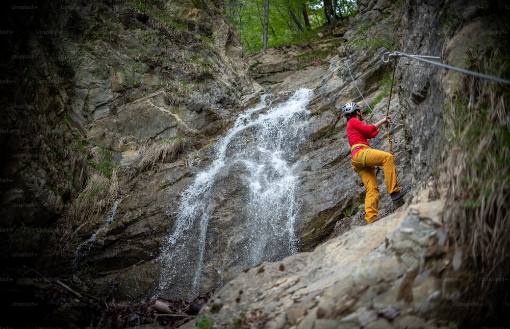a man climbing up the side of a mountain next to a waterfall