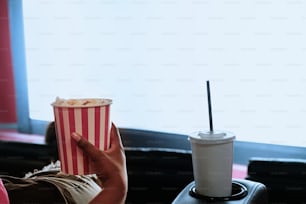 eine Person, die eine Tasse Popcorn und ein Getränk in der Hand hält