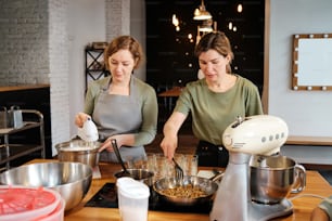 Zwei Frauen in einer Küche, die Essen miteinander mischen