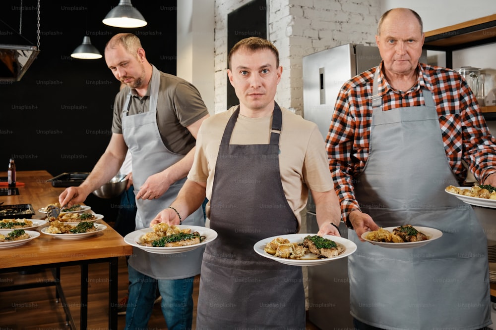 three men in aprons holding plates of food