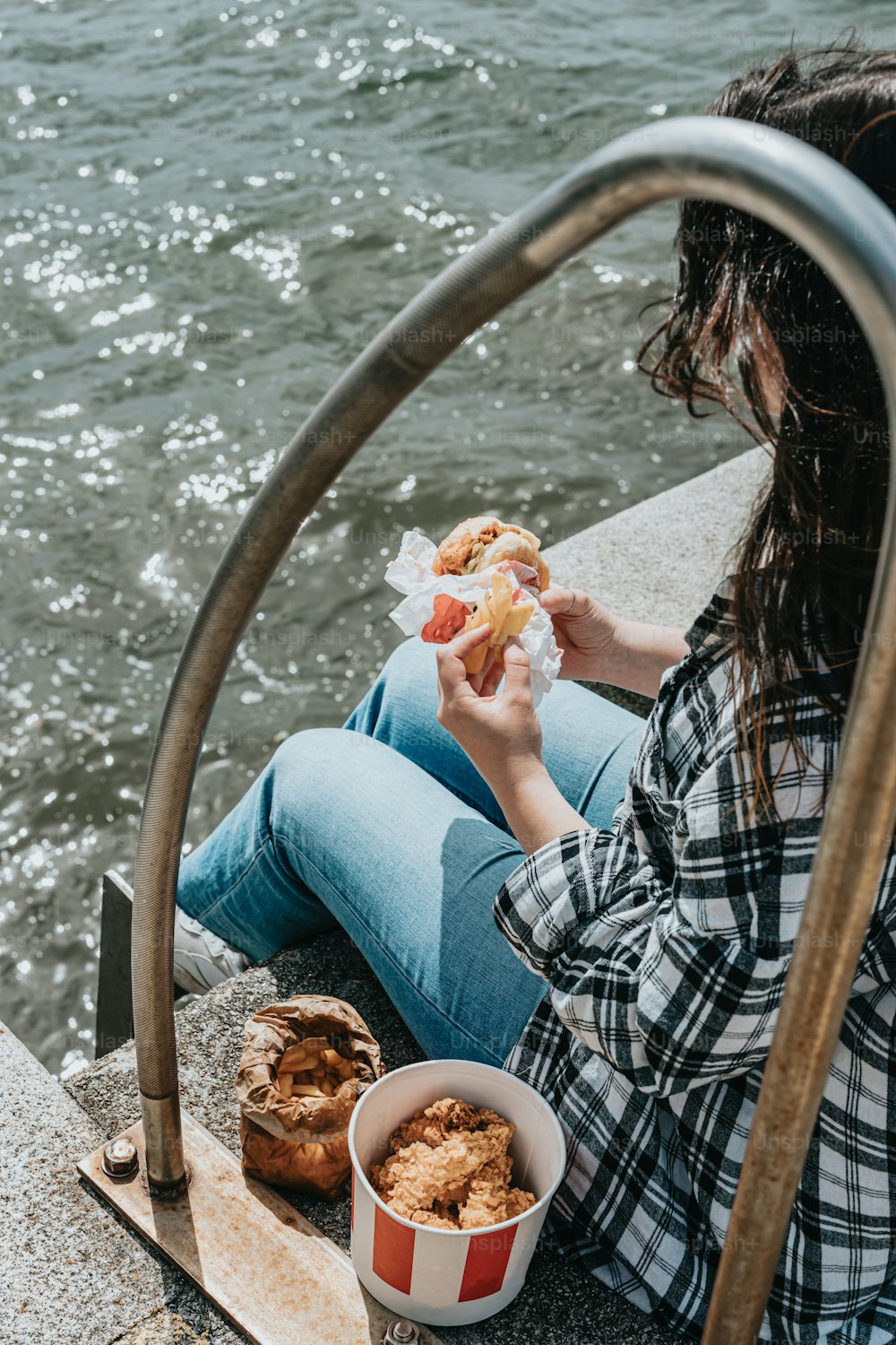 a woman eating a hot dog next to a body of water