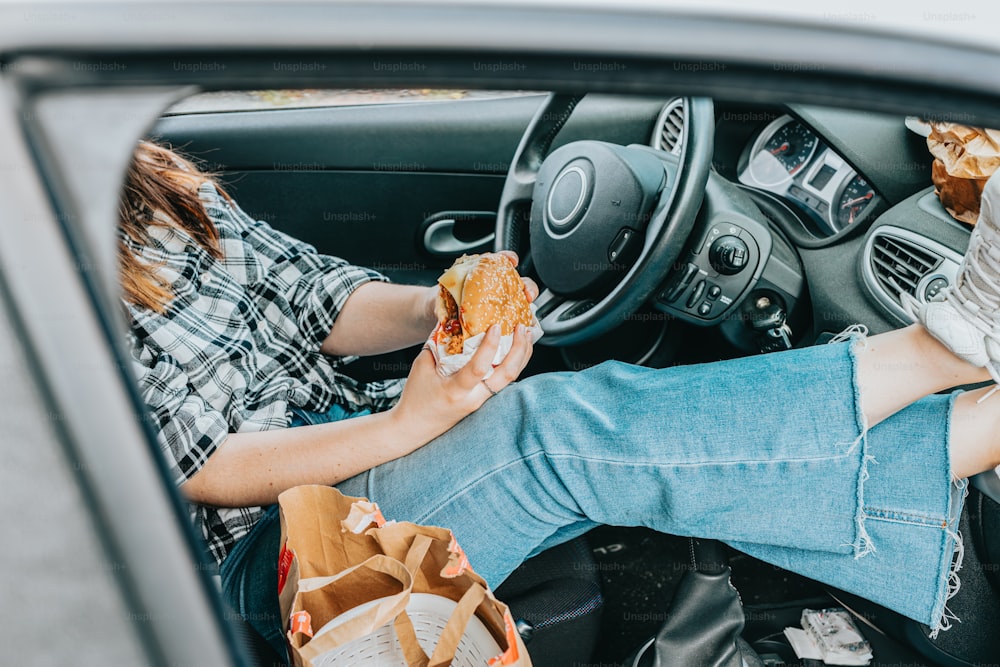uma mulher sentada em um carro comendo um sanduíche