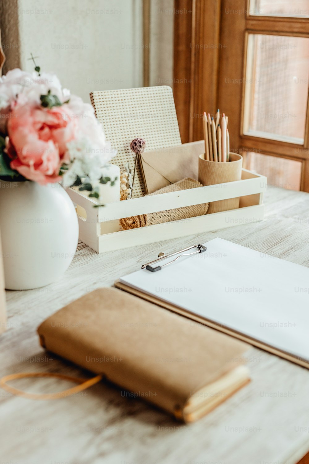 uma mesa com bloco de notas, porta-canetas e um vaso de flores