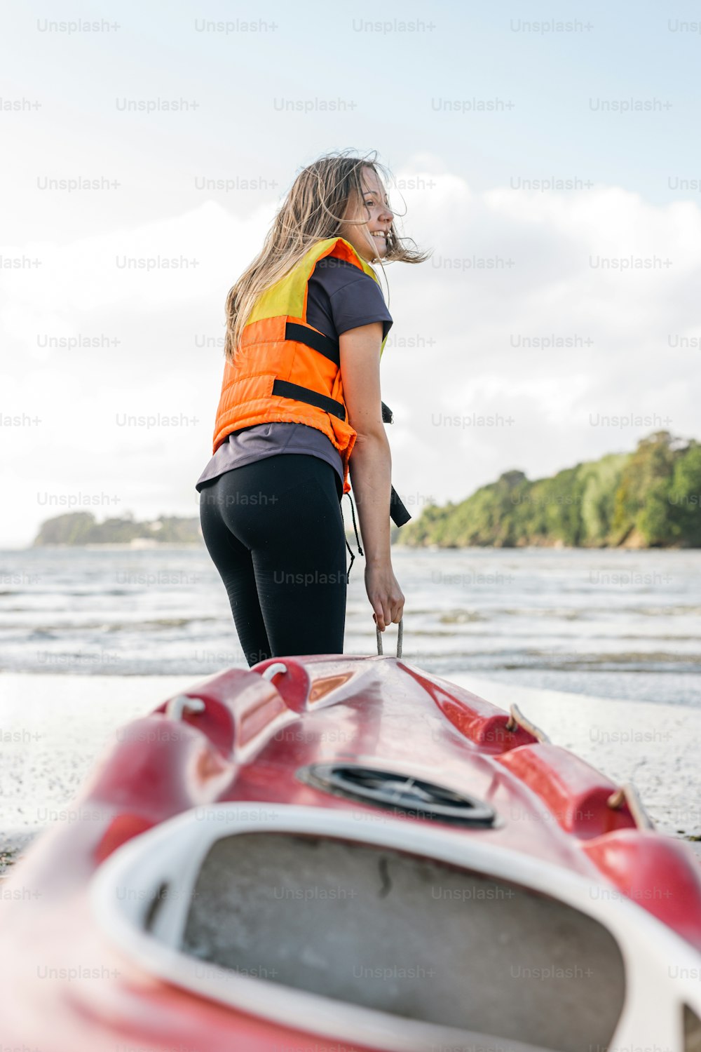 Una mujer parada junto a un kayak rojo en una playa