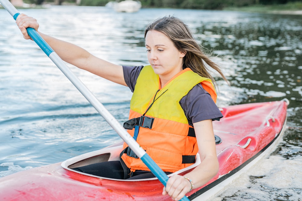 a woman in an orange life jacket paddling a red kayak