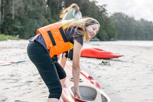 a woman in an orange life jacket is putting something in a red kayak