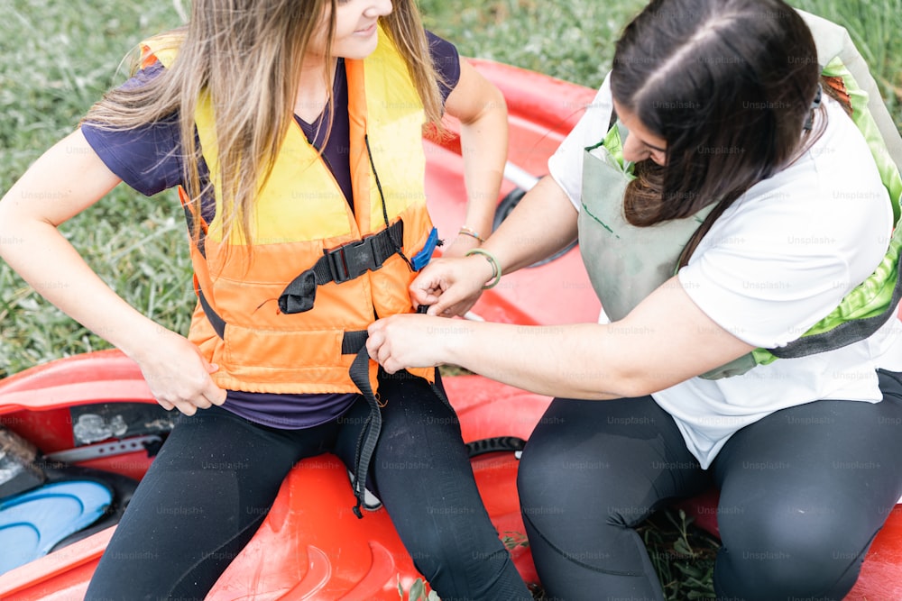a woman helping another woman put on a life jacket