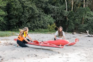 two women sitting on a beach next to a kayak