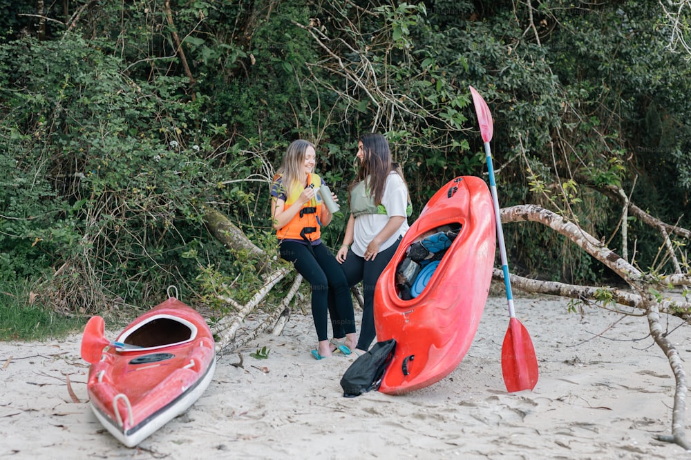 two women standing on a beach next to kayaks
