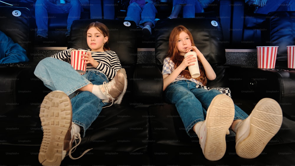 two girls sitting on a couch watching a movie