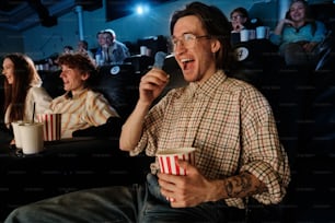 Ein Mann, der in einem Kino sitzt und eine Tasse Popcorn in der Hand hält