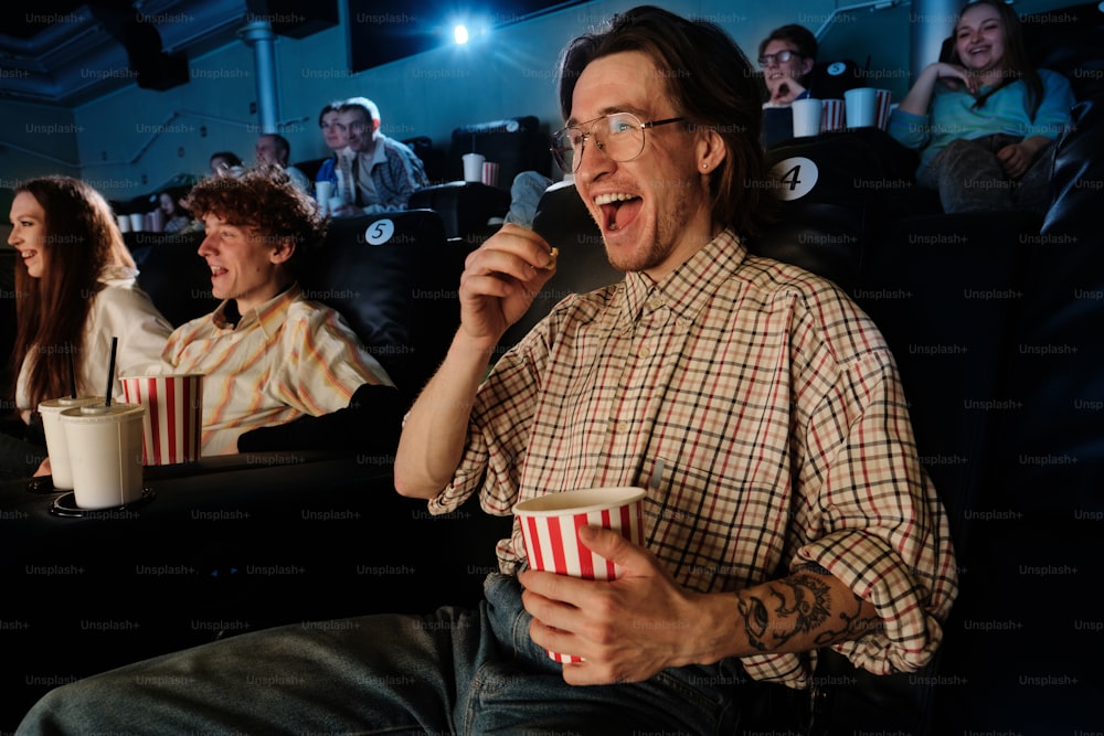a man sitting in a movie theater holding a cup of popcorn