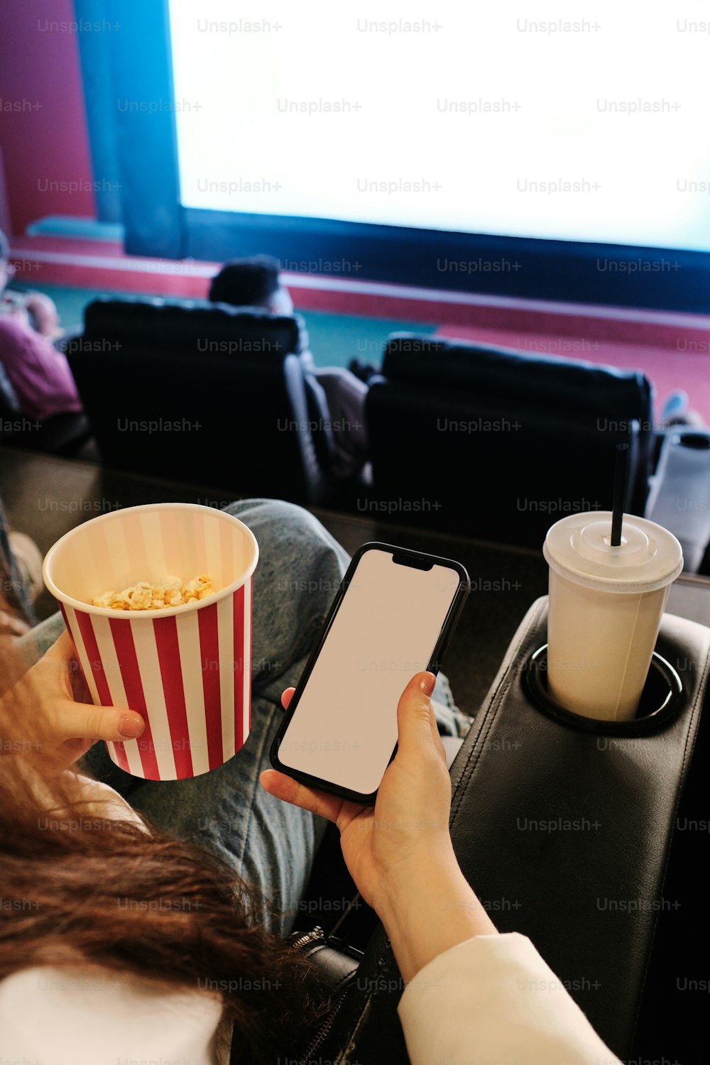 a woman holding a smart phone while sitting in front of a movie screen