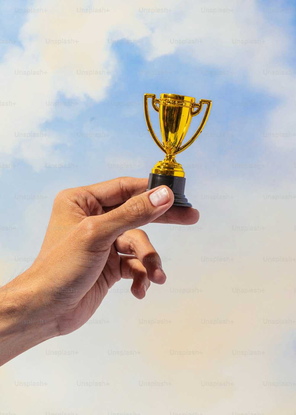 a hand holding a gold trophy against a blue sky