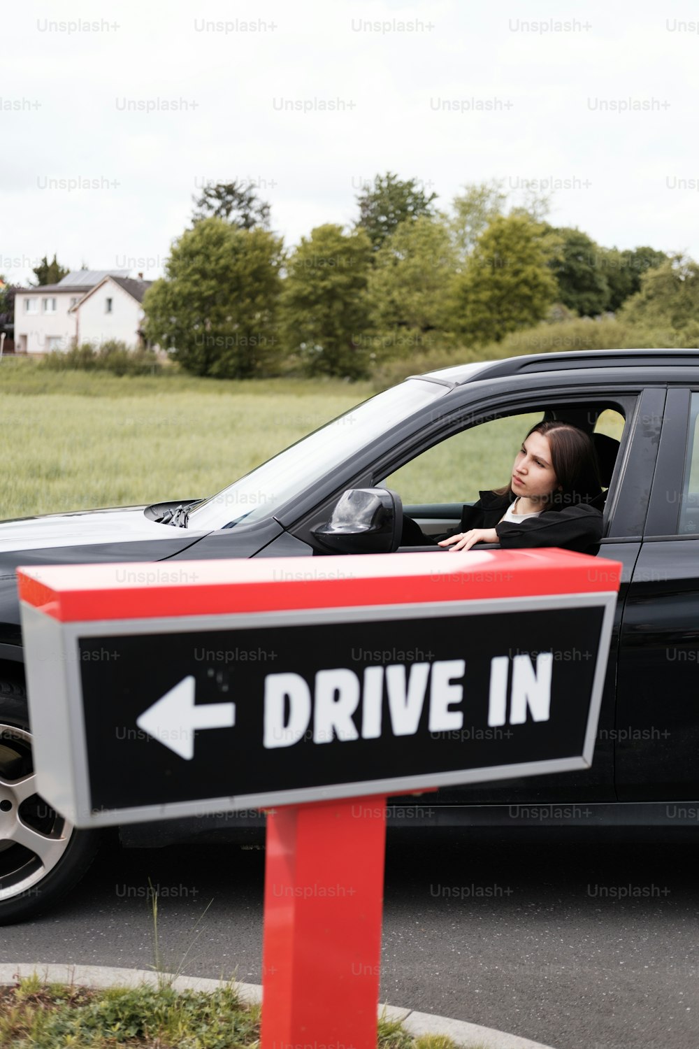 a woman sitting in a car with a drive in sign in front of her